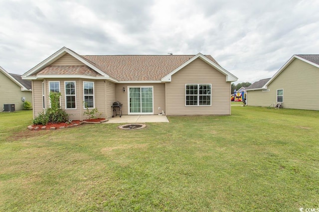 rear view of property with a lawn, central air condition unit, a patio area, and a fire pit