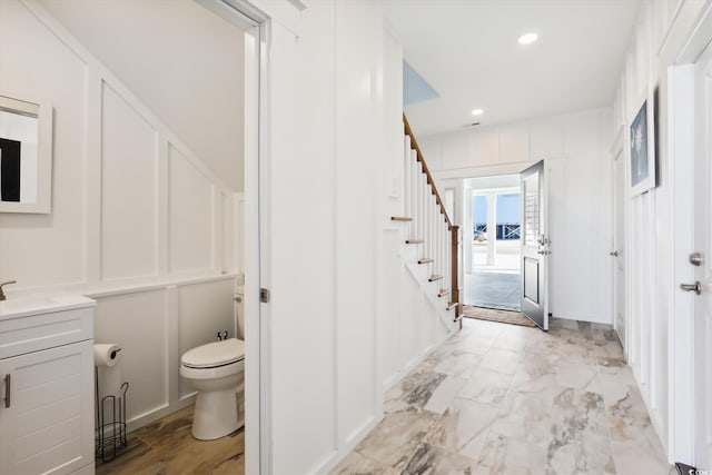 bathroom with vanity, recessed lighting, a decorative wall, toilet, and marble finish floor