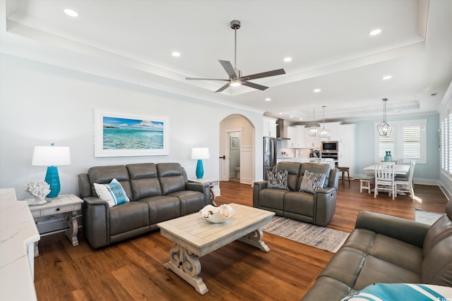 living room featuring arched walkways, dark wood finished floors, and a tray ceiling