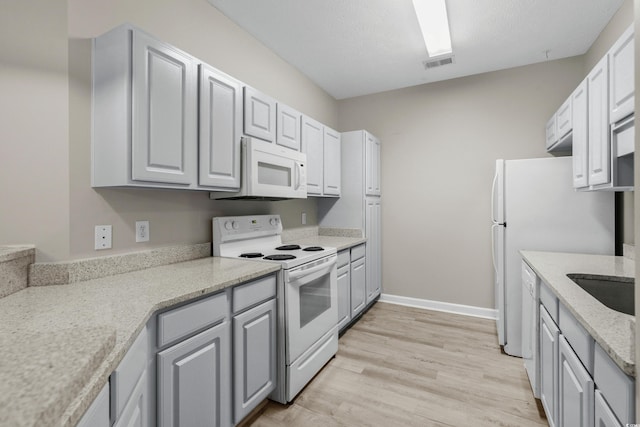 kitchen featuring light wood-type flooring, light stone counters, white appliances, and sink