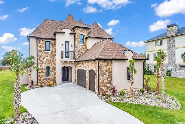 french provincial home with stucco siding, stone siding, a balcony, driveway, and a front yard