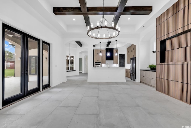 unfurnished living room with coffered ceiling, arched walkways, a towering ceiling, and an inviting chandelier