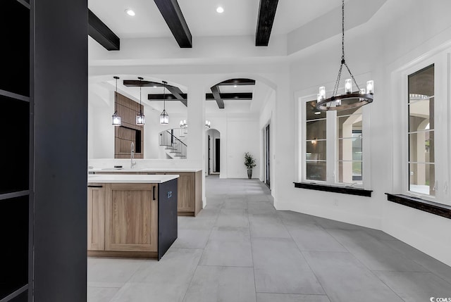 kitchen featuring light countertops, beamed ceiling, arched walkways, hanging light fixtures, and an inviting chandelier