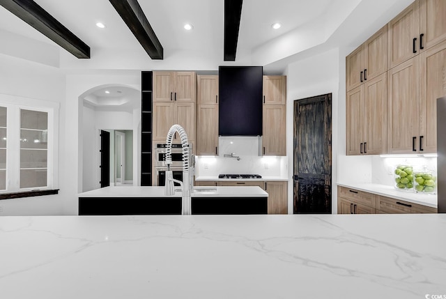 kitchen featuring double oven, light brown cabinetry, beamed ceiling, and gas cooktop