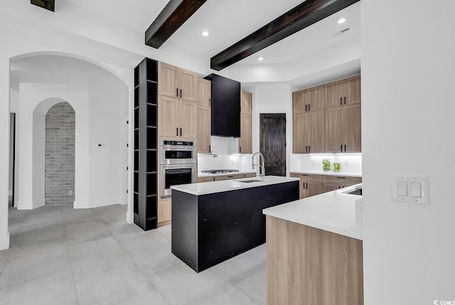 kitchen featuring light countertops, beamed ceiling, a kitchen island with sink, stainless steel appliances, and a sink