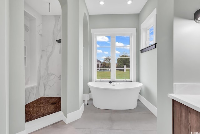 bathroom featuring baseboards, a marble finish shower, a freestanding tub, and vanity