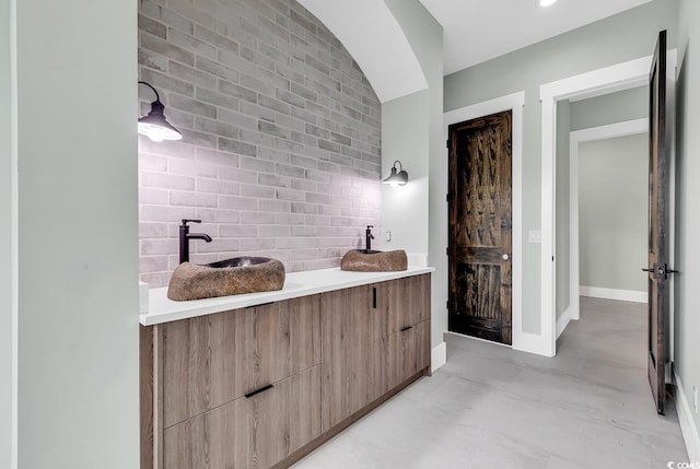 bathroom with finished concrete flooring, baseboards, brick wall, and vanity