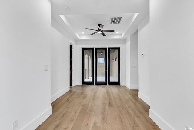 spare room with ceiling fan, light wood-type flooring, french doors, and a raised ceiling