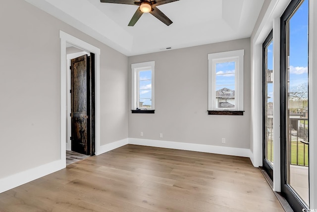 spare room featuring a tray ceiling, light wood-type flooring, a ceiling fan, and a wealth of natural light