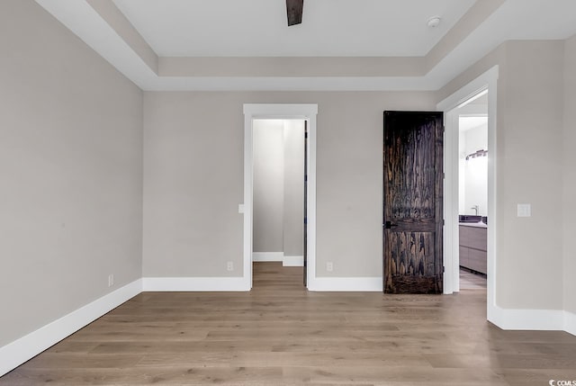 unfurnished bedroom with a tray ceiling and light hardwood / wood-style floors