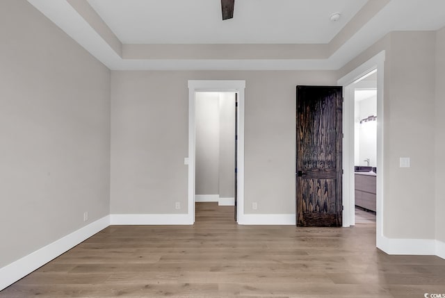 unfurnished room featuring a tray ceiling, baseboards, and light wood-type flooring