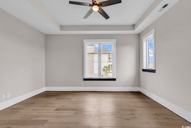 unfurnished room with wood finished floors, ceiling fan, a raised ceiling, and visible vents
