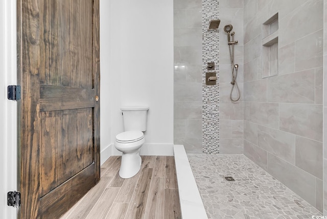 full bath with baseboards, a tile shower, toilet, and wood finished floors