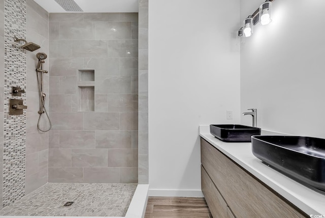 bathroom with baseboards, double vanity, a tile shower, wood finished floors, and a sink