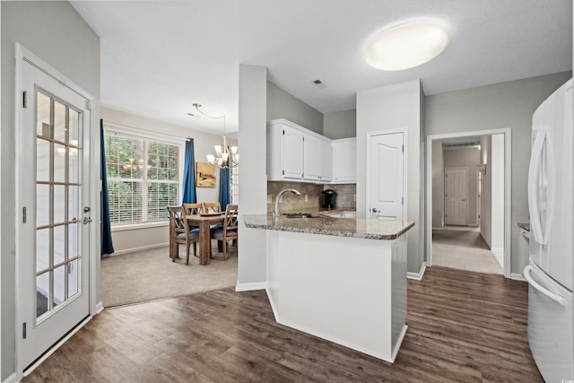 kitchen featuring light stone counters, white cabinets, kitchen peninsula, dark hardwood / wood-style floors, and white fridge