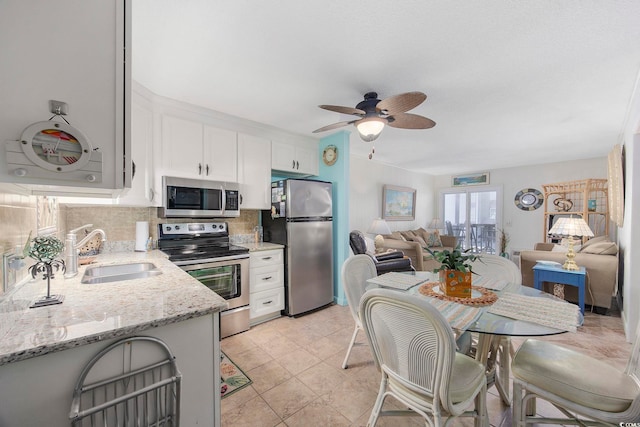 kitchen featuring appliances with stainless steel finishes, sink, backsplash, white cabinets, and light stone counters