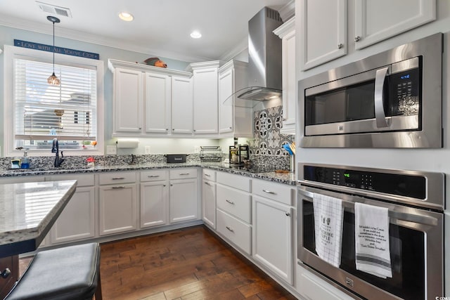 kitchen featuring appliances with stainless steel finishes, sink, dark stone countertops, white cabinets, and wall chimney exhaust hood