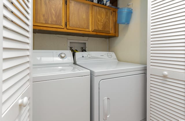 clothes washing area with cabinets and washing machine and clothes dryer