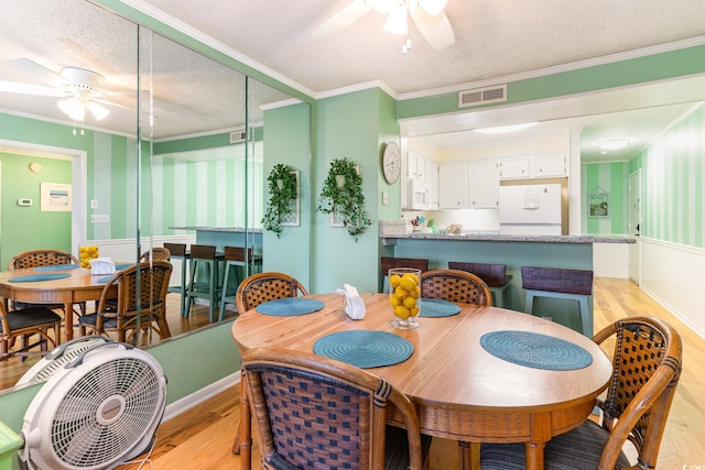 dining room featuring light hardwood / wood-style floors, crown molding, ceiling fan, and a textured ceiling