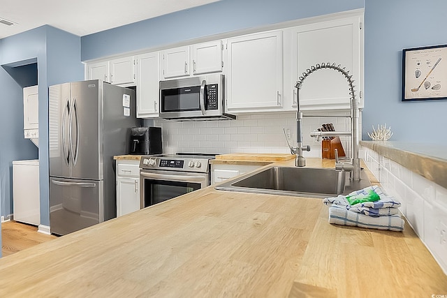 kitchen featuring white cabinets, sink, stacked washing maching and dryer, stainless steel appliances, and decorative backsplash