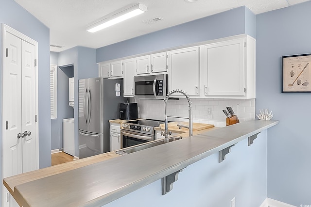 kitchen with backsplash, white cabinetry, stainless steel appliances, a breakfast bar area, and stacked washer and dryer