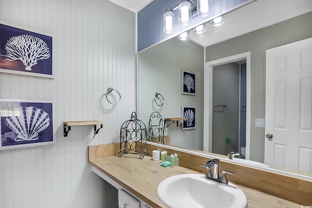 bathroom with vanity, wooden walls, and toilet