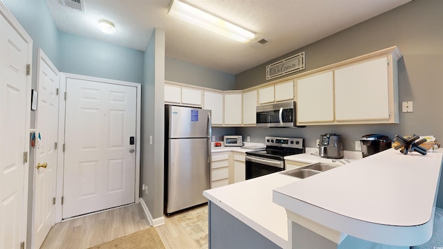 kitchen with kitchen peninsula, appliances with stainless steel finishes, a textured ceiling, sink, and light hardwood / wood-style floors