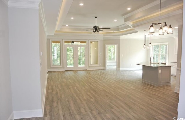 unfurnished living room with ceiling fan, sink, hardwood / wood-style flooring, a tray ceiling, and crown molding