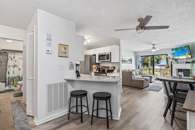 kitchen featuring appliances with stainless steel finishes, white cabinets, a kitchen bar, kitchen peninsula, and light hardwood / wood-style flooring