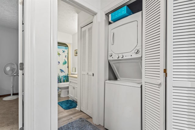 laundry area featuring stacked washer / drying machine, a textured ceiling, and light wood-type flooring