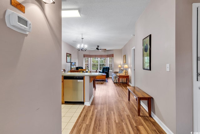 kitchen with light hardwood / wood-style floors, a breakfast bar area, ceiling fan with notable chandelier, a textured ceiling, and dishwasher