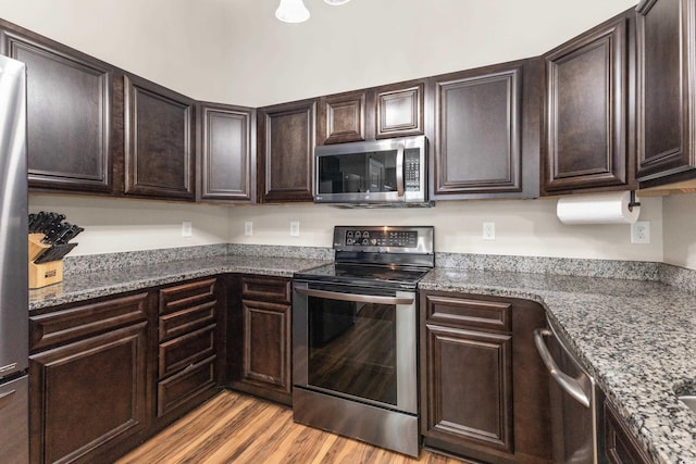 kitchen with light hardwood / wood-style flooring, appliances with stainless steel finishes, dark stone counters, and dark brown cabinetry