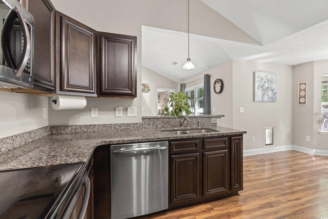 kitchen featuring appliances with stainless steel finishes, dark stone countertops, sink, hanging light fixtures, and vaulted ceiling