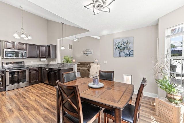 dining area featuring a towering ceiling, ceiling fan with notable chandelier, light hardwood / wood-style flooring, and sink