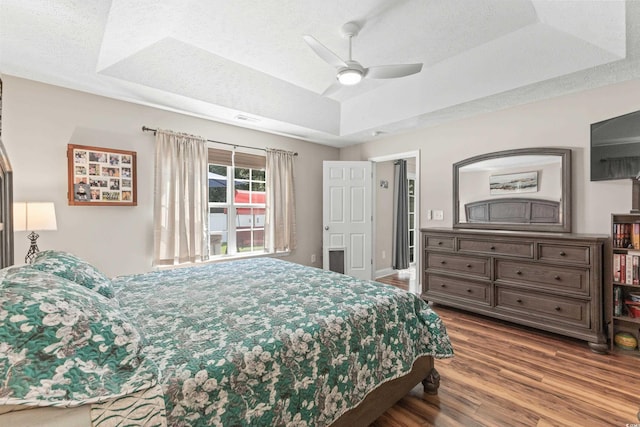 bedroom featuring a raised ceiling, ceiling fan, a textured ceiling, and hardwood / wood-style flooring