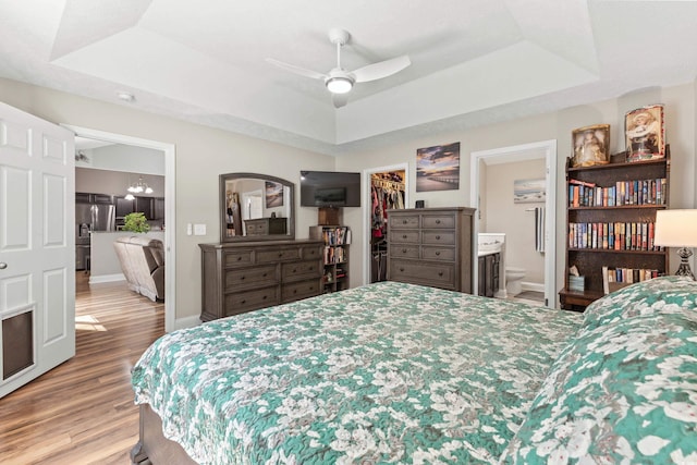 bedroom featuring ceiling fan, connected bathroom, a walk in closet, and a raised ceiling