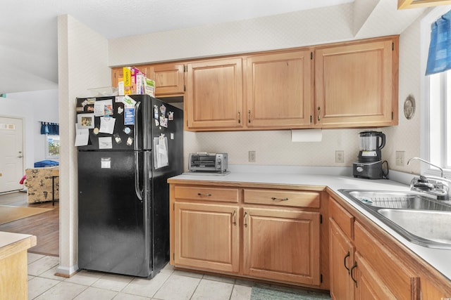 kitchen with black refrigerator, light tile patterned floors, a healthy amount of sunlight, and sink