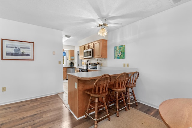 kitchen with a kitchen bar, appliances with stainless steel finishes, kitchen peninsula, a textured ceiling, and light hardwood / wood-style flooring