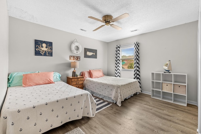 bedroom with ceiling fan, wood-type flooring, and a textured ceiling