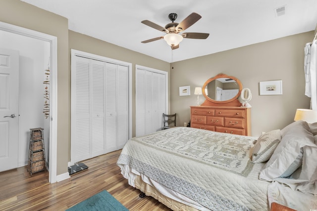 bedroom with hardwood / wood-style floors, ceiling fan, and multiple closets