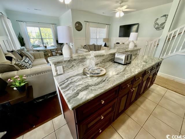 kitchen with light tile patterned flooring, a center island, ceiling fan, and light stone counters