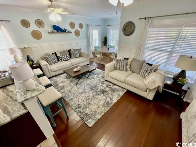 living room featuring ceiling fan, ornamental molding, dark wood-type flooring, and a healthy amount of sunlight