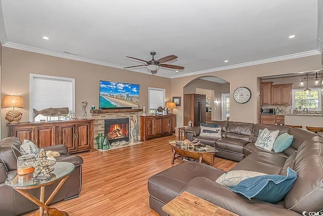 living room with a fireplace, ornamental molding, ceiling fan, and light hardwood / wood-style flooring