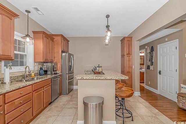 kitchen featuring appliances with stainless steel finishes, a kitchen island, a kitchen bar, light hardwood / wood-style flooring, and sink