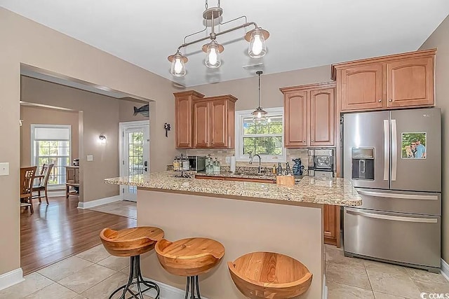 kitchen with a breakfast bar, decorative light fixtures, stainless steel fridge, and a wealth of natural light