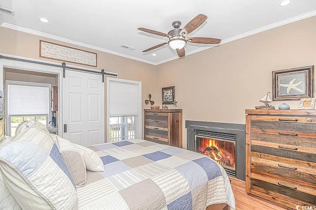 bedroom with ceiling fan, a barn door, crown molding, and light hardwood / wood-style floors