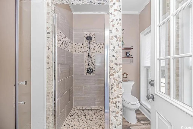 bathroom featuring wood-type flooring, ornamental molding, toilet, and tiled shower