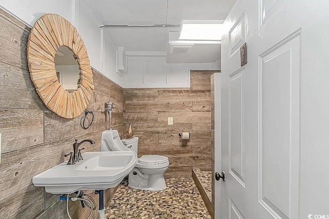 bathroom with wooden walls, toilet, and sink