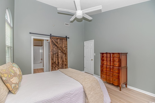 bedroom with ceiling fan, a high ceiling, a barn door, ensuite bathroom, and light wood-type flooring