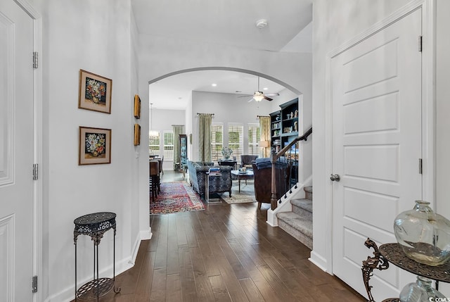 entryway featuring arched walkways, ceiling fan, dark wood-type flooring, stairway, and baseboards
